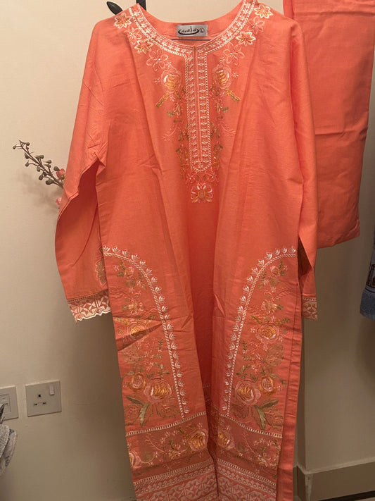 Orange embroidered garment on a hanger against a neutral background
